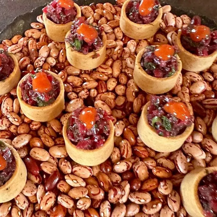 Tartelettes garnies de tartare et de tomate confite, présentées sur un lit de haricots secs