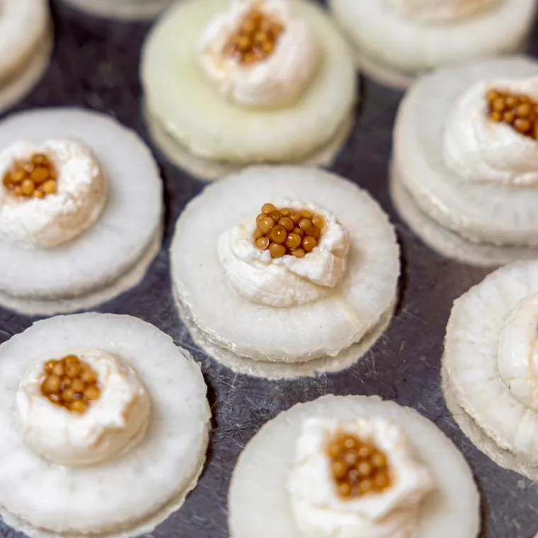 Bouchées rondes nappées de crème et garnies de perles dorées, sur plateau sombre